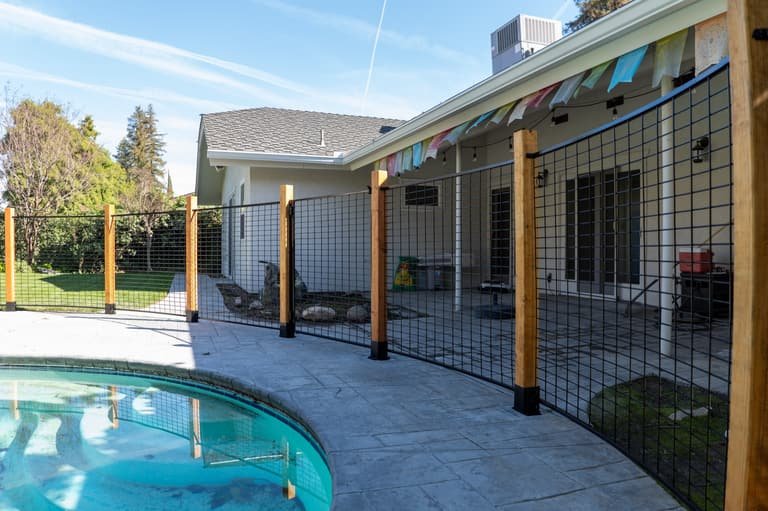 Hog panel fence with gate sections and wood posts near a patio
