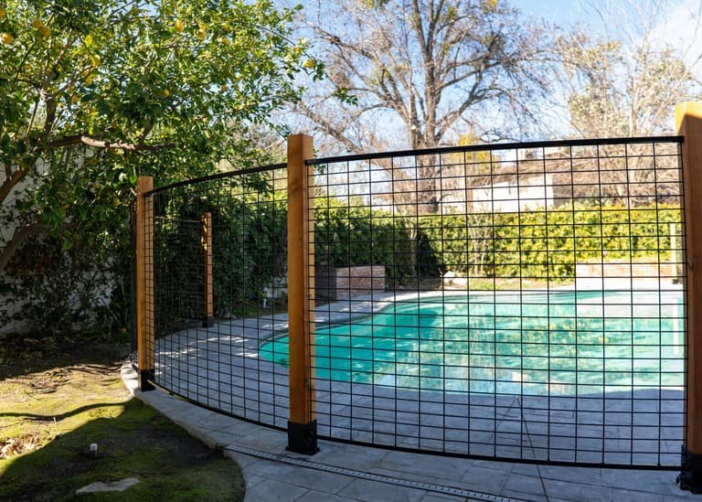 Black welded wire hog panel fence section with wood posts near a pool